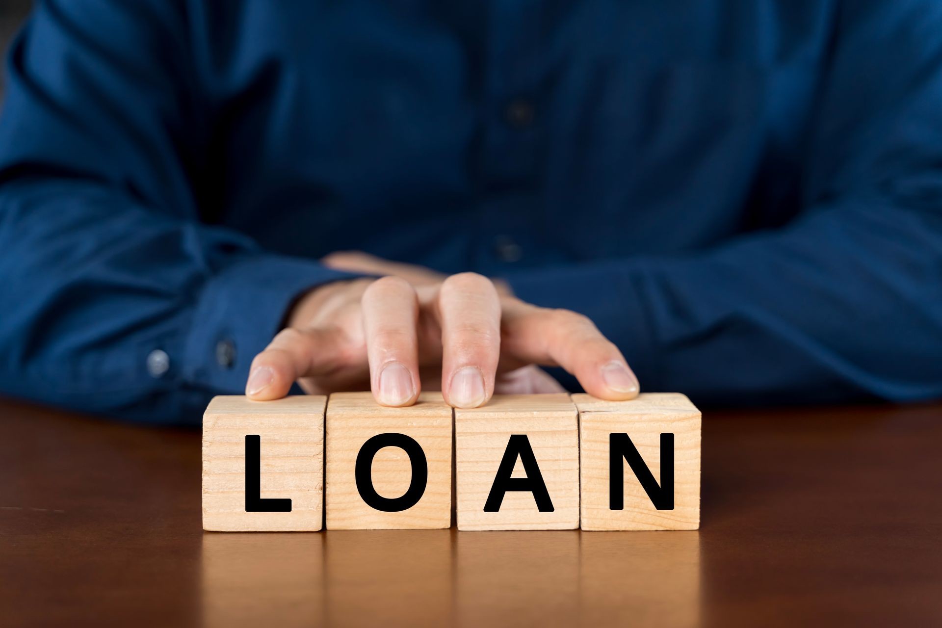 Person in blue shirt arranging wooden blocks spelling 'loan' on a table.